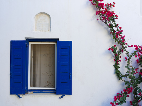Mediterranean style white house exterior with blue door and window, flowering tree and romantic seating area. Traditional patio of Santorini.