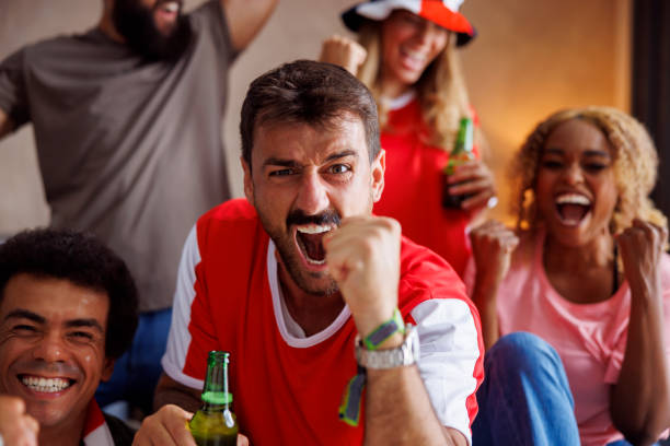 Football fans having fun cheering and celebrating while watching game on TV Group of cheerful football fans having fun cheering and celebrating after their team scoring a goal while watching world championship game on TV at home football league stock pictures, royalty-free photos & images