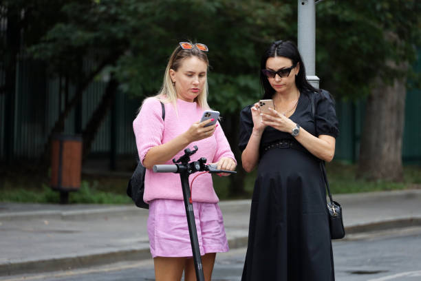 duas mulheres em roupas de verão usando celulares parados na rua da cidade - smart phone iphone women mobile phone - fotografias e filmes do acervo