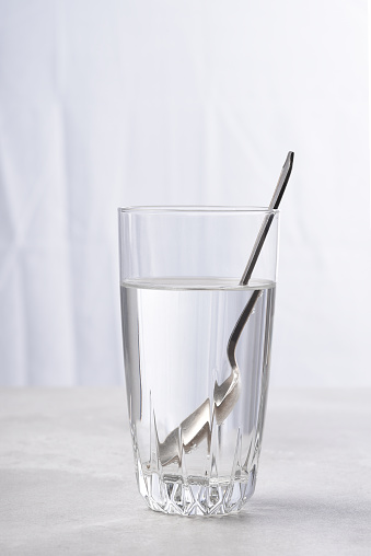 High key image of a teaspoon in glass of water with refraction.