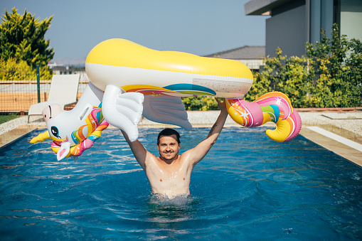 Man lifting inflatable unicorn float in swimming pool