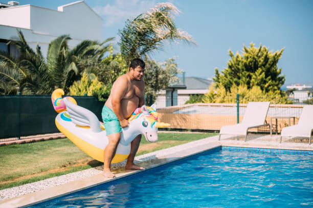 istock Man jumping to pool with inflatable unicorn 1413678471