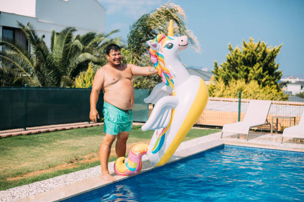 istock Man holding inflatable unicorn at the pool 1413678639