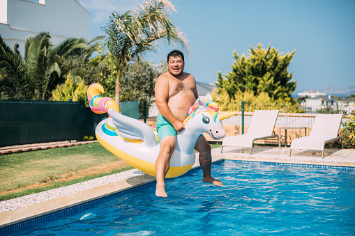 Fat man jumping to pool with inflatable unicorn