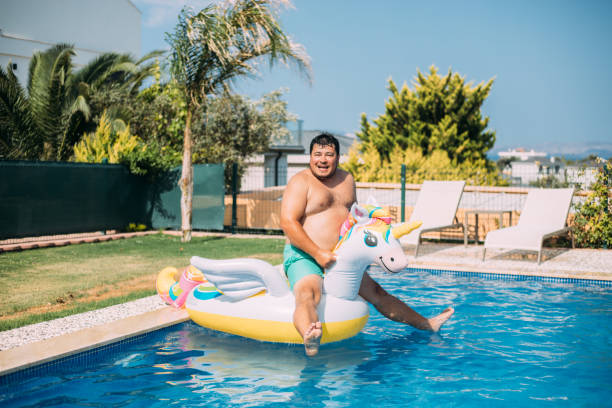 istock Man jumping to pool with inflatable unicorn 1413678722