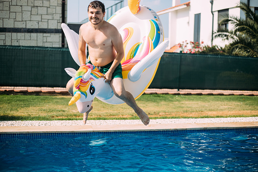 Man jumping into the pool with inflatable unicorn float