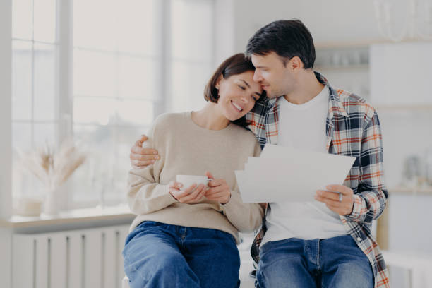 istock Caring husband embraces wife with love, have glad expressions, holds paper documents, discuss banking procedures, study bills, drink tea or coffee, pose indoor, enjoy calm domestic atmosphere 1413679785