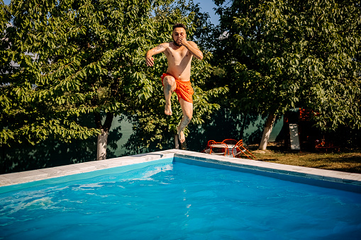 Young adult man jumping into pool, 30-35 years old.