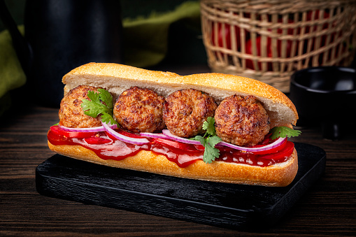 Meatball sandwich with tomato, onion, parsley, barbecue sauce. Dark background.
