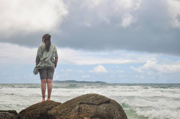 istock Young woman standing alone on the rocks looking at the beach 1413683561