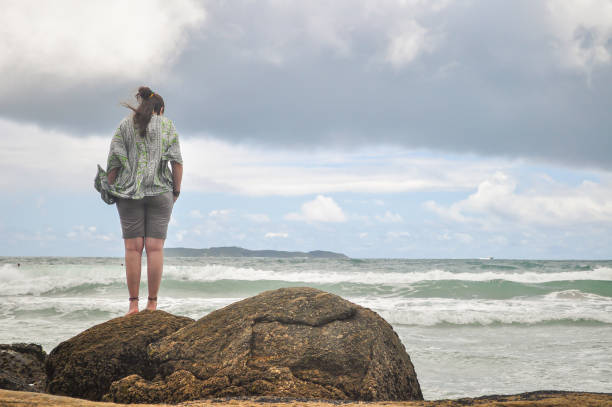 istock Young woman standing alone on the rocks looking at the beach 1413683602