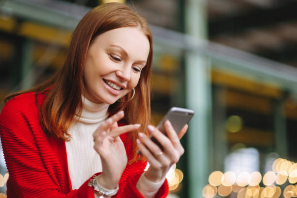 Positive pleased female model uses mobile phone data, uses chat application, holds modern cell phone, smiles positively, dressed in red coat, waits for answer or call from boyfriend, has brown hair modelo femenino satisfecho positivo utiliza datos del teléfono móvil, utiliza la aplicación de chat, tiene teléfono celular moderno, sonríe positivamente, vestido con abrigo rojo, espera la respuesta o la llamada de novio, tiene el pelo castaño