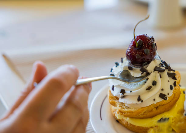 ケーキの上からチェリーを取るティースプーンを持つ女性の手のクローズアップビュー - unhealthy eating cherry chocolate close up ストックフォトと画像