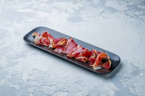 Spanish Jamon (Hamon), parma ham sliced on plate on white concrete table Spanish Jamon (Hamon), parma ham sliced on plate on white concrete table uncooked bacon stock pictures, royalty-free photos & images