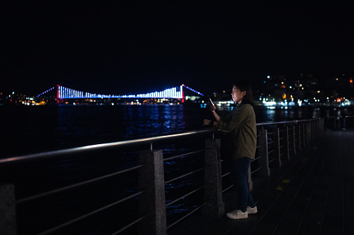 A young female tourist is using her smart phone in city at night.