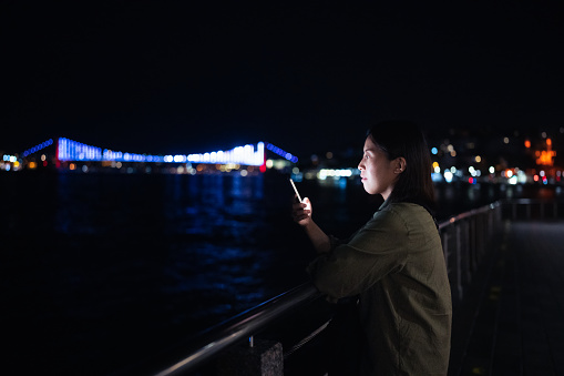 A young female tourist is using her smart phone in city at night.