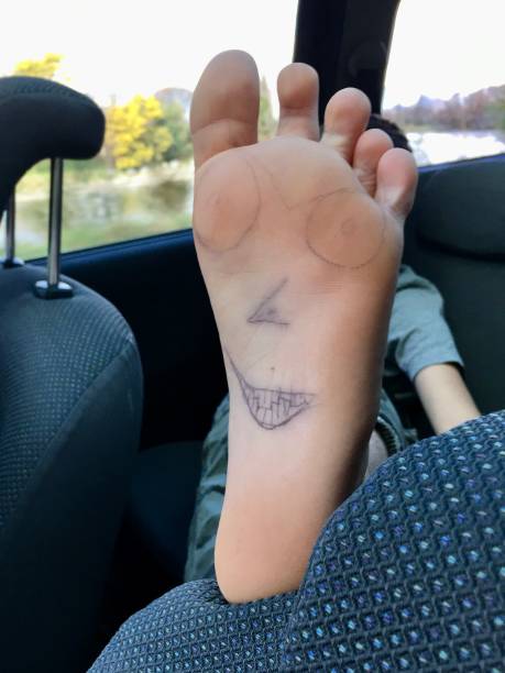 A boy holds up his foot in a car to reveal a face drawn on his foot.