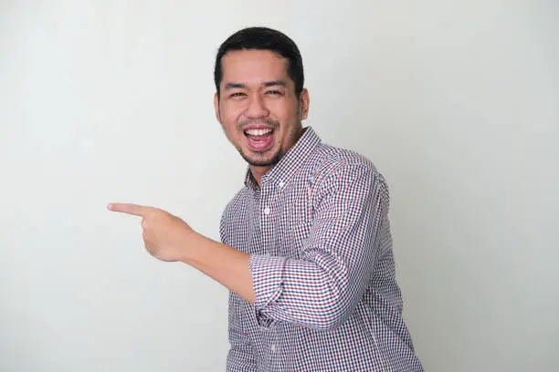 Adult Asian man looking camera with happy expression while pointing to the right