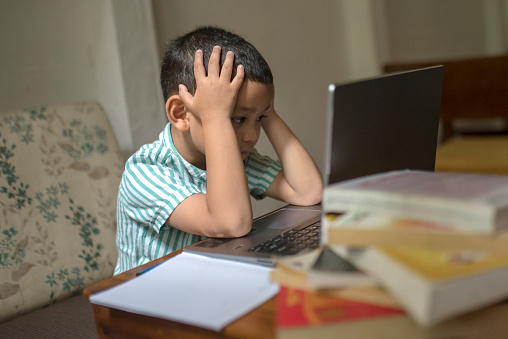Asian kid showing confused expression in front of laptop