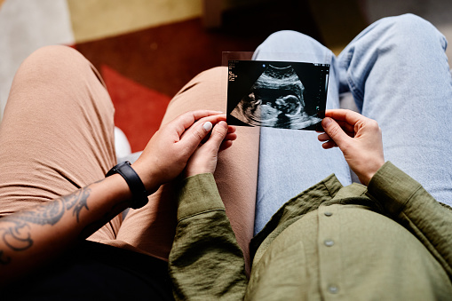 Close up of tattooed gay couple with pregnant young woman looking at ultrasound image of baby, same sex family