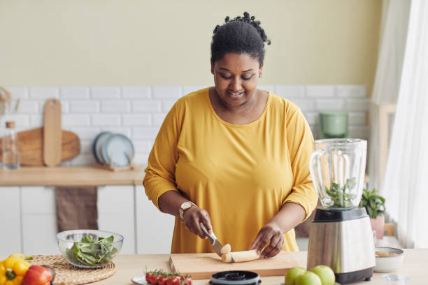 Black Woman Cooking at Home Portrait of smiling black woman cutting bananas while making healthy meal in kitchen and filming cooking video, copy space huge black woman pictures stock pictures, royalty-free photos & images