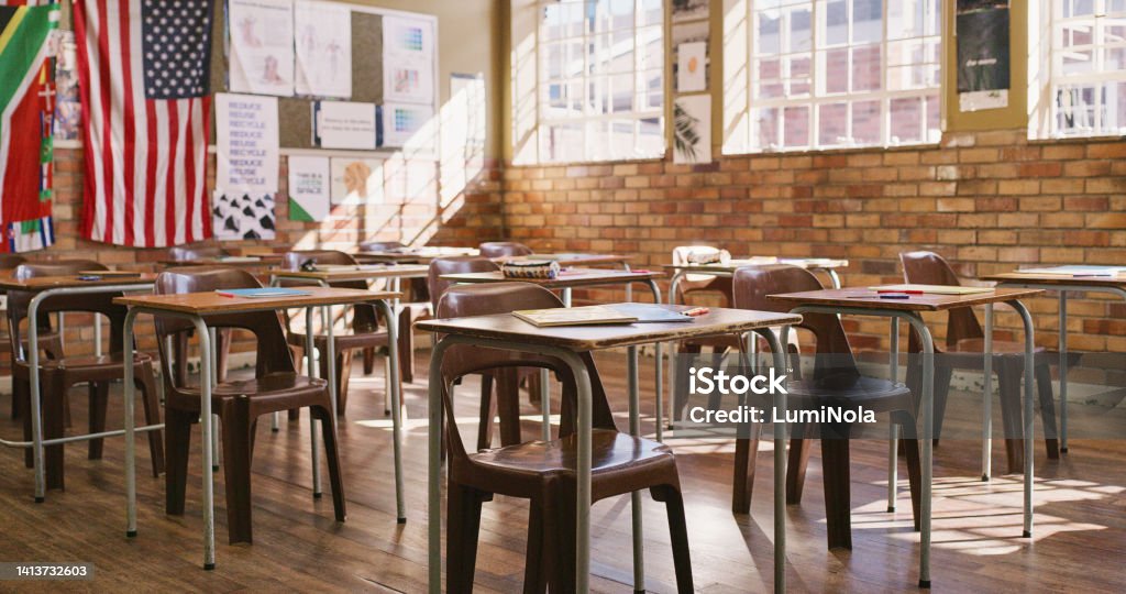 Empty classroom with wooden desks, table and chairs for a lesson inside an elementary, middle or high school. Education, learning and knowledge to study for teaching academic students, kids and youth Arranging Stock Photo