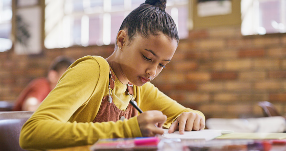 Young girl at school taking a test in the classroom. Female student busy with an exam, focusing and writing an essay. Small teenager in learning and education in a class room.