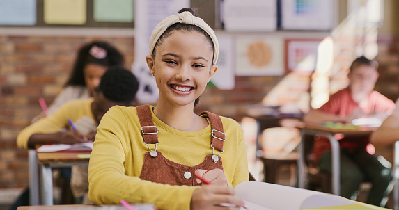 Young, smiling and happy school girl writing notes in class. Elementary student learning and taking down information with excitement. Education and gaining knowledge through creativity and fun