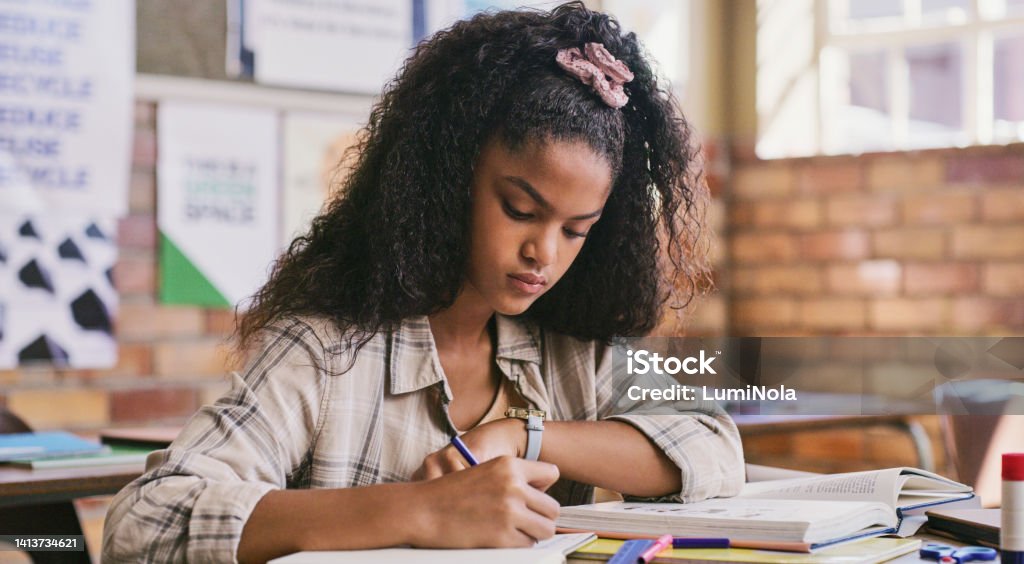 Study, classroom and education for child writing essay or exam at school. Serious teenage student learning and reading from textbook while making notes in her notebook during test or lesson in class Back to School Stock Photo