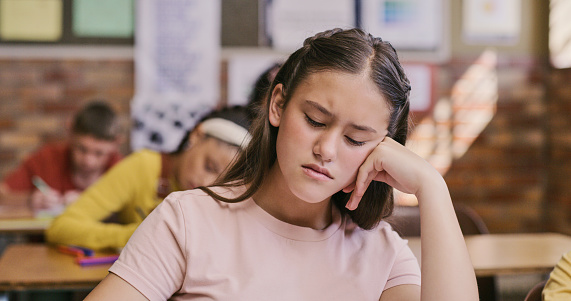 Sad, upset and depressed student sitting in classroom and struggling with education and learning at her school. Bored and tired girl with ADHD or autism unable to concentrate during lesson in class