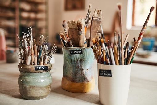 Paint brushes, supplies and equipment in jars at a school, art class or creative workshop. Utensils for painting, designing or creating on a table for artwork, painters or creativity in a studio