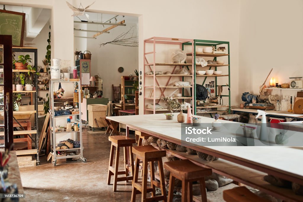 Interior of modern pottery studio or creative workshop space filled with shelves and table of hand made fine art and ceramics. Clay molding and sculpture class for culture crafts with wood chairs. Art Stock Photo