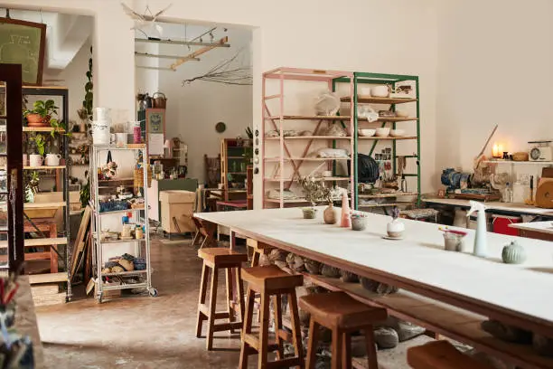 Photo of Interior of modern pottery studio or creative workshop space filled with shelves and table of hand made fine art and ceramics. Clay molding and sculpture class for culture crafts with wood chairs.