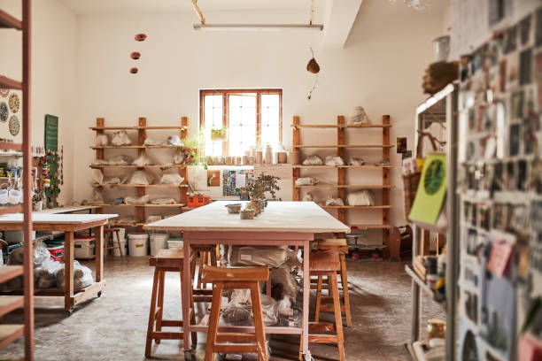 An empty clay pottery store or workshop with a potter's desk and handmade craft collection on a shelf in an empty shop during the day. Craftsman workplace with ceramic pots, plates and jars on a rack una tienda o taller de cerámica de arcilla vacío con un escritorio de alfarero y una colección de artesanía hecha a mano en un estante en una tienda vacía durante el día. lugar de trabajo de artesano con ollas, platos y frascos de cerámica en un est