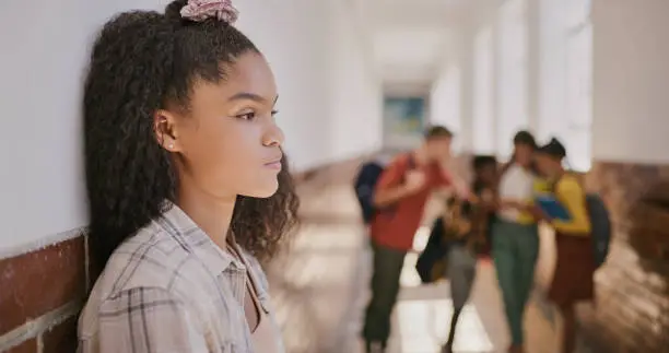 Young sad teenage girl feeling lonely and excluded at school. Female outside classroom and thinking about teen problems, bullying or trouble feeling depressed and anxiety.