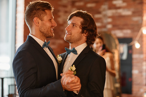 Waist up portrait of young gay couple dancing together during wedding ceremony, copy space