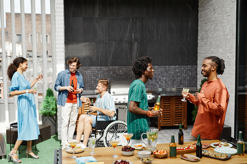 Diverse group of friends enjoying party at outdoor terrace and communicating, including person in wheelchair