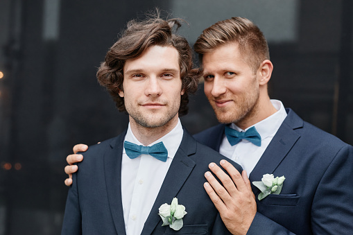 Portrait of two young men posing as couple and smiling at camera during wedding ceremony