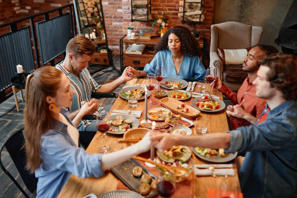 High angle view at diverse group of young people holding hands at table saying grace during dinner party
