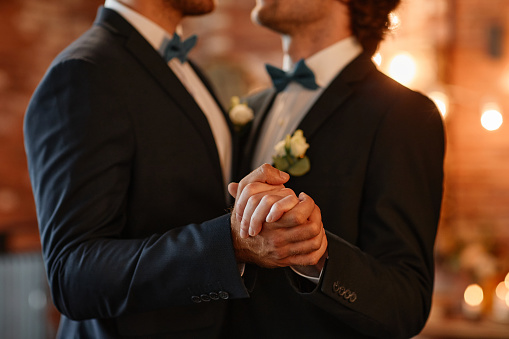 Close up of male gay couple dancing together during wedding ceremony and holding hands, copy space