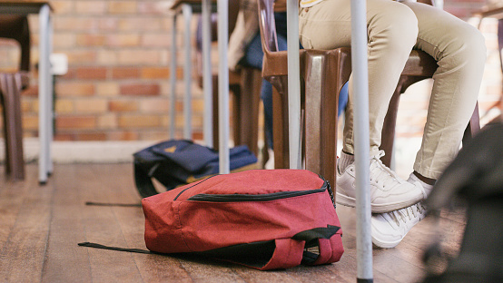 Legs of children sitting in a class at an elementary school learning and getting a quality education. Students learning in a classroom with their backpacks or bags on the floor
