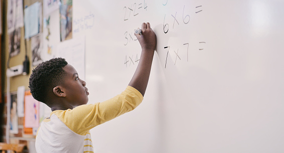 Educación, aula y aprendizaje mientras el estudiante negro resuelve una ecuación matemática y escribe respuestas en la pizarra. Niño de escuela inteligente haciendo una suma multiplicada y calculando una solución en clase photo