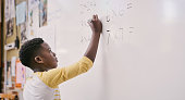 istock Education, classroom and learning while black student solve a maths equation and write answers on the whiteboard. Smart little school boy doing multiply sum and calculating a solution in class 1413741751