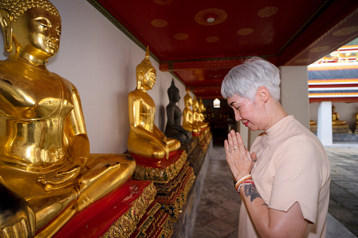 Senior woman is solo traveler. She is enjoy to explore her world. Asia culture. Bangkok Thailand. Wat pho is public temple for praying Buddha.