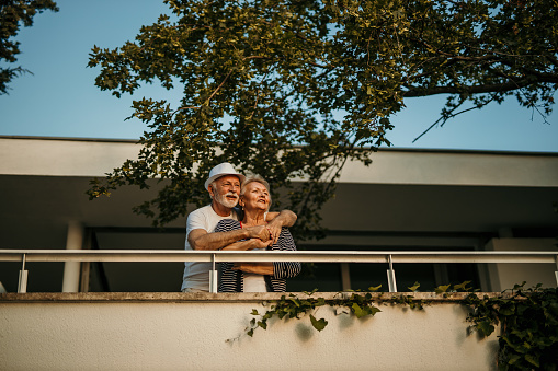 Low angle view of a lovely Active Seniors on a Beautiful Sunny Day standing on a balcony and enjoying the sunset.