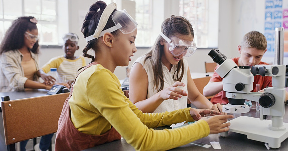 Children in a science class at school doing an experiment wearing safety goggles. Smart, clever and intelligent students learning biology or chemistry lesson in a classroom