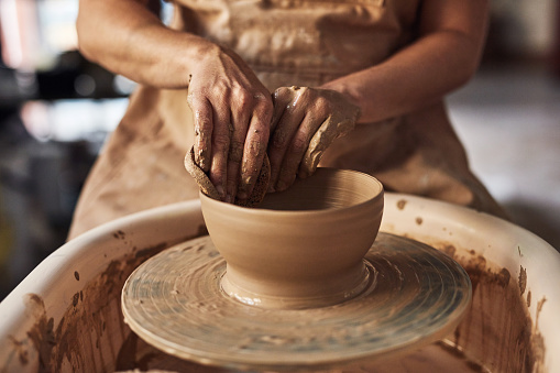 Pottery artist, designer or employee molding an object with clay at a factory, studio or art class. Ceramist, potter or person creating, shaping and making a bowl with hands at an artistic workshop