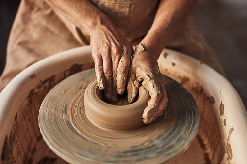 Art, manufacturing and creative female hands working with wet clay to design, shape and create ceramic bowl on a pottery wheel in her workshop. Artistic worker making handmade crafts as a hobby