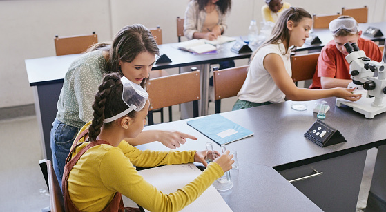 Science class teacher helping student in classroom. Education, learning and development to become young scientists. Patient, listening and interested educator watching over learners working in class.