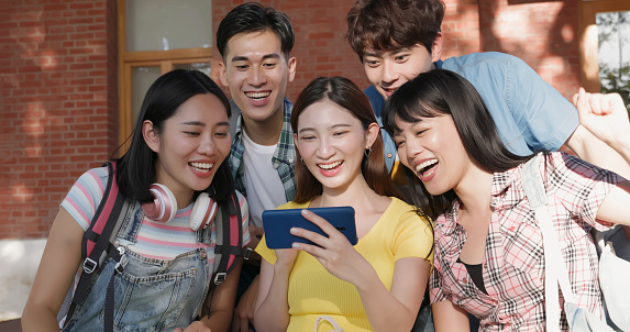 young asian students watching sport streaming on smartphone happily with fist gesture in campus